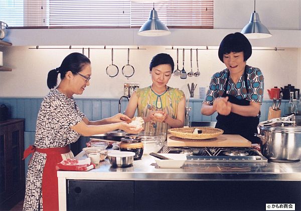 写真あり。マサコ、サチエ、ミドリが作業テーブルでおにぎりを握っている写真